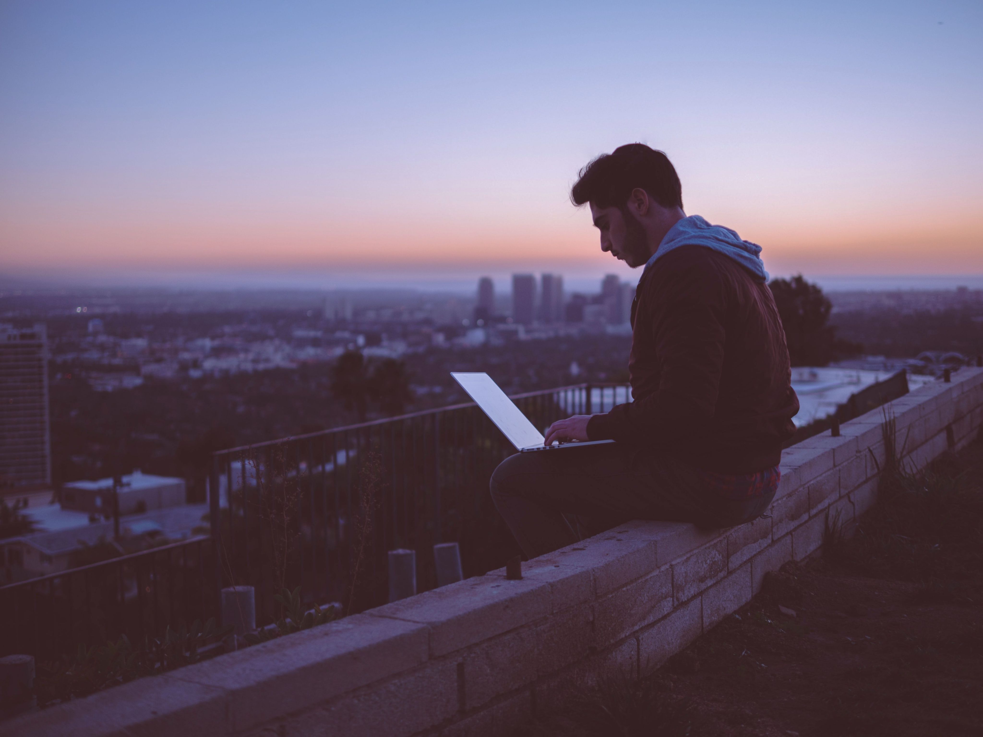 man sitting on concrete brick with opened laptop on his lap