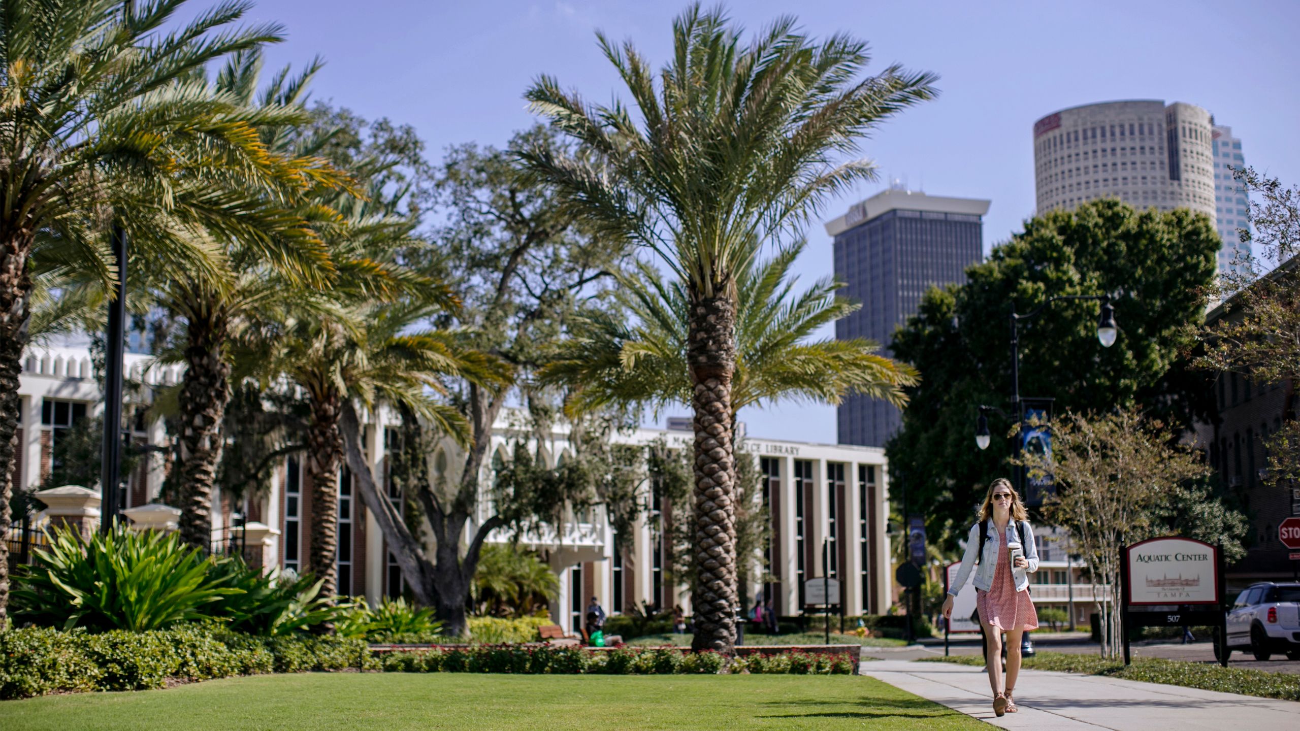 A student walks through the center of campus with downtown Tampa buildings in the background 